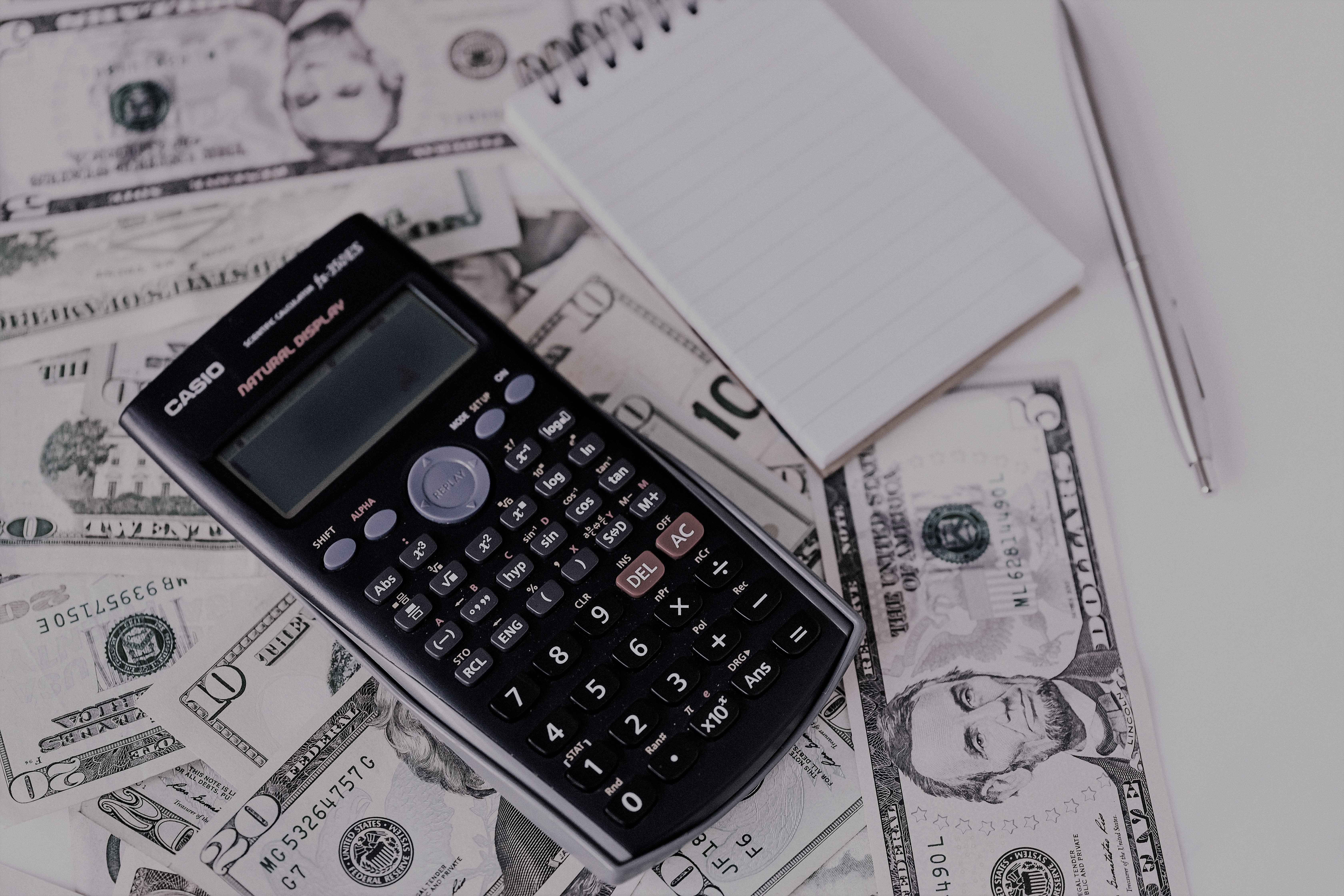 Calculator and notepad placed on USA dollars stack